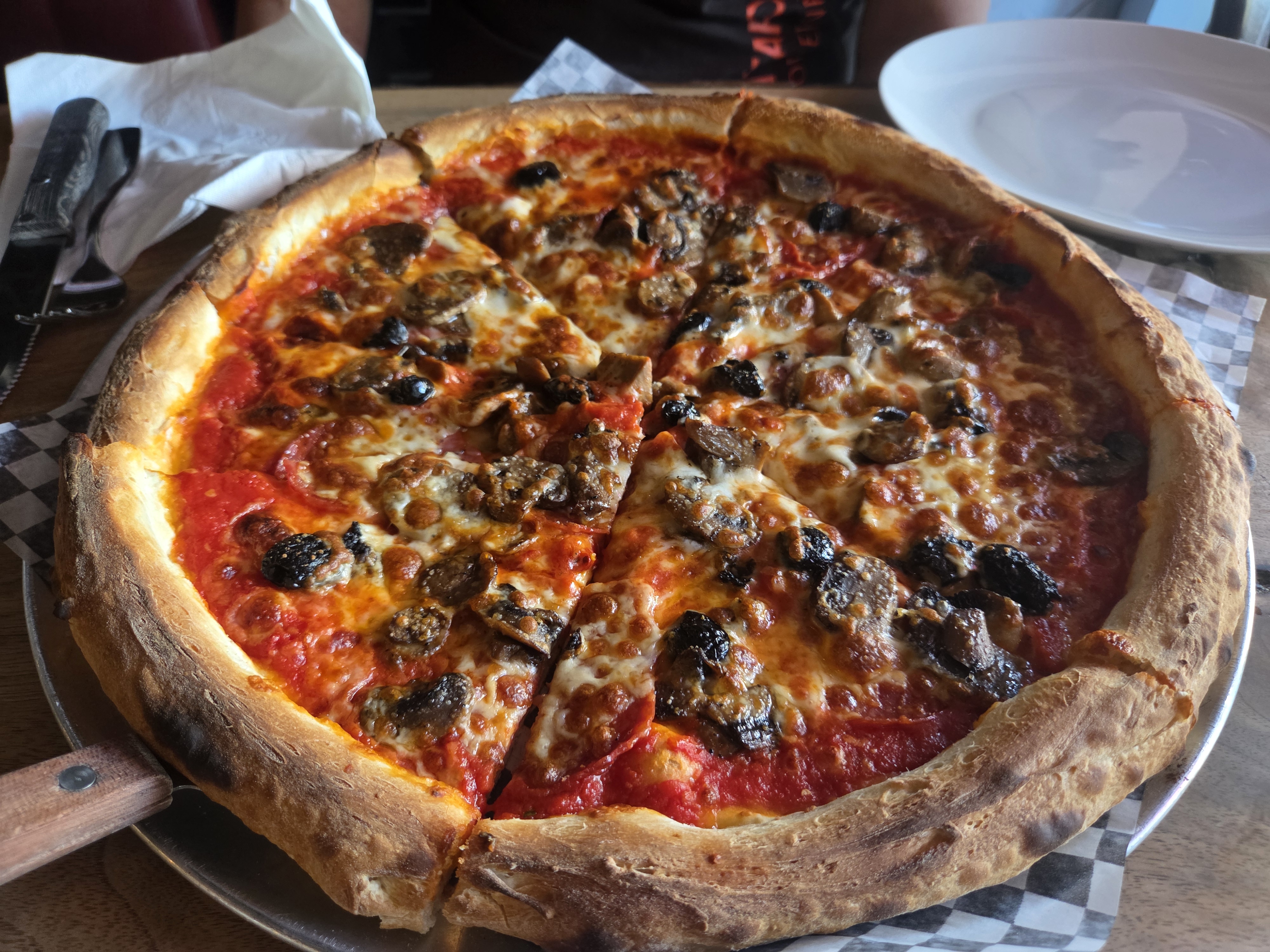 A freshly baked pizza with sausage and mushroom toppings, cut into slices, resting on a metal tray.