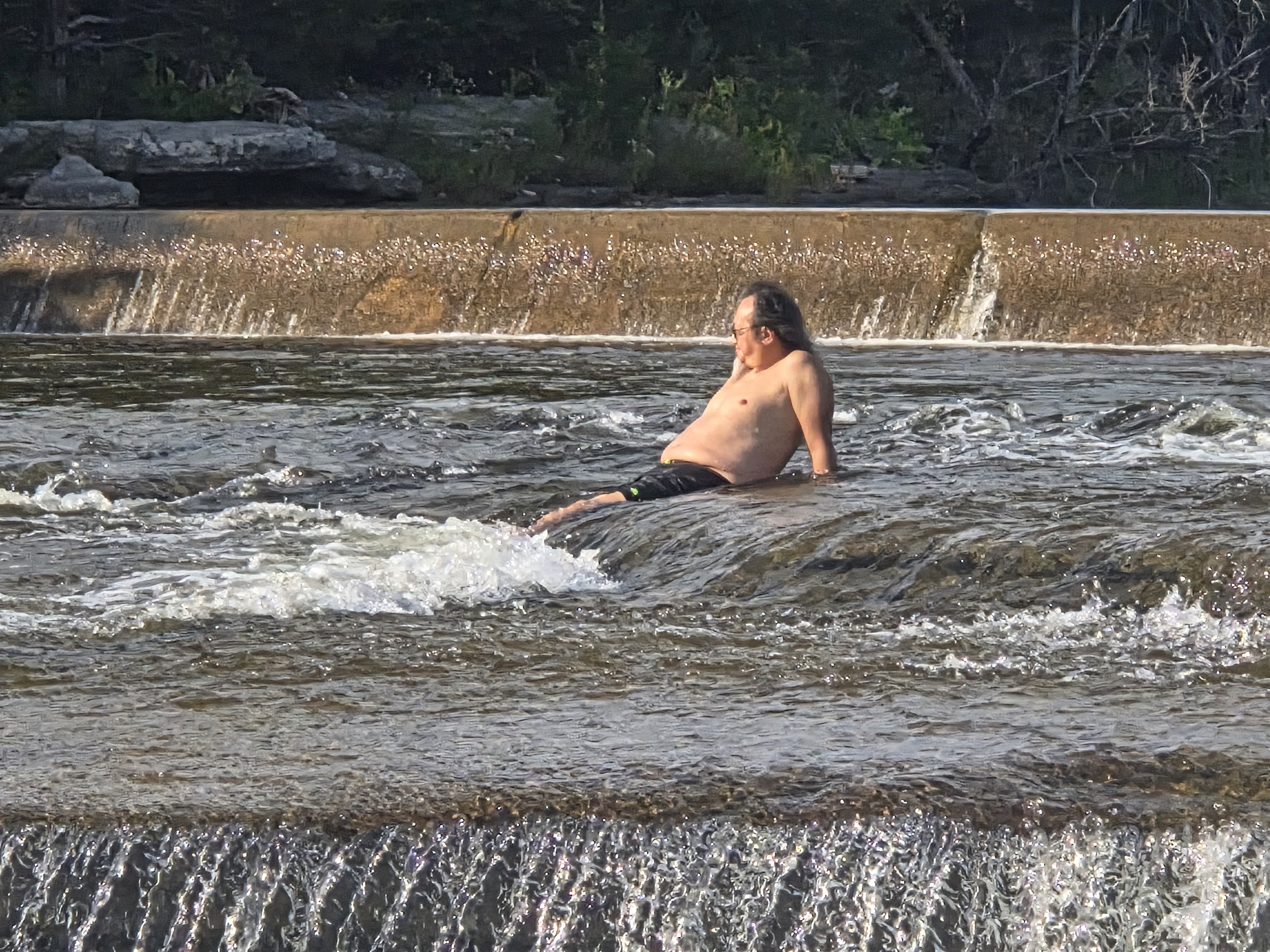 A person relaxing in a river, sitting on a rock with water flowing around them, enjoying the natural scenery.
